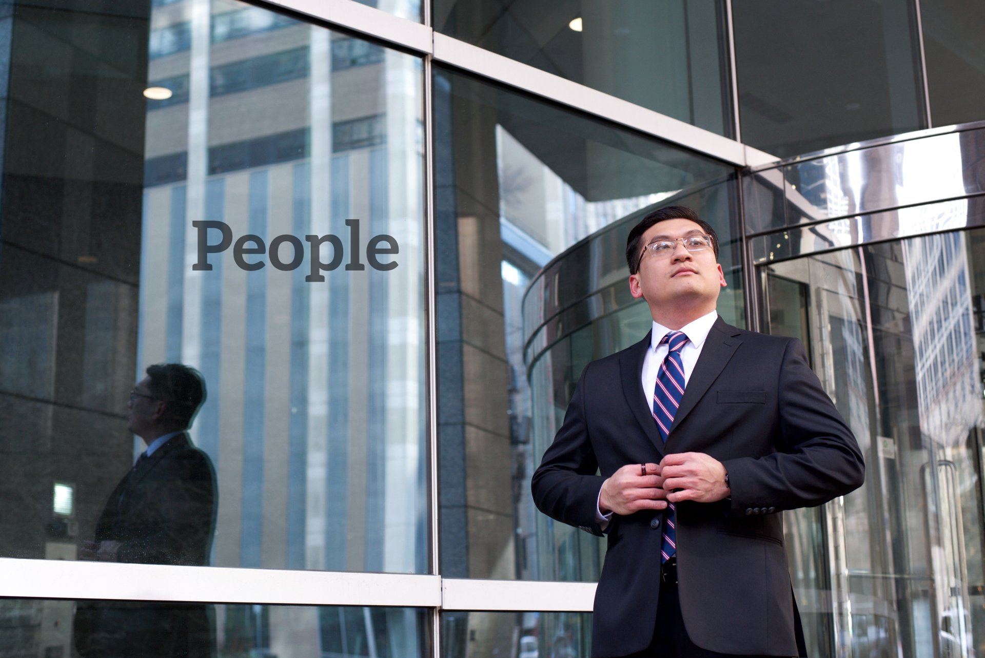 A man in a suit stands in front of a building that says people