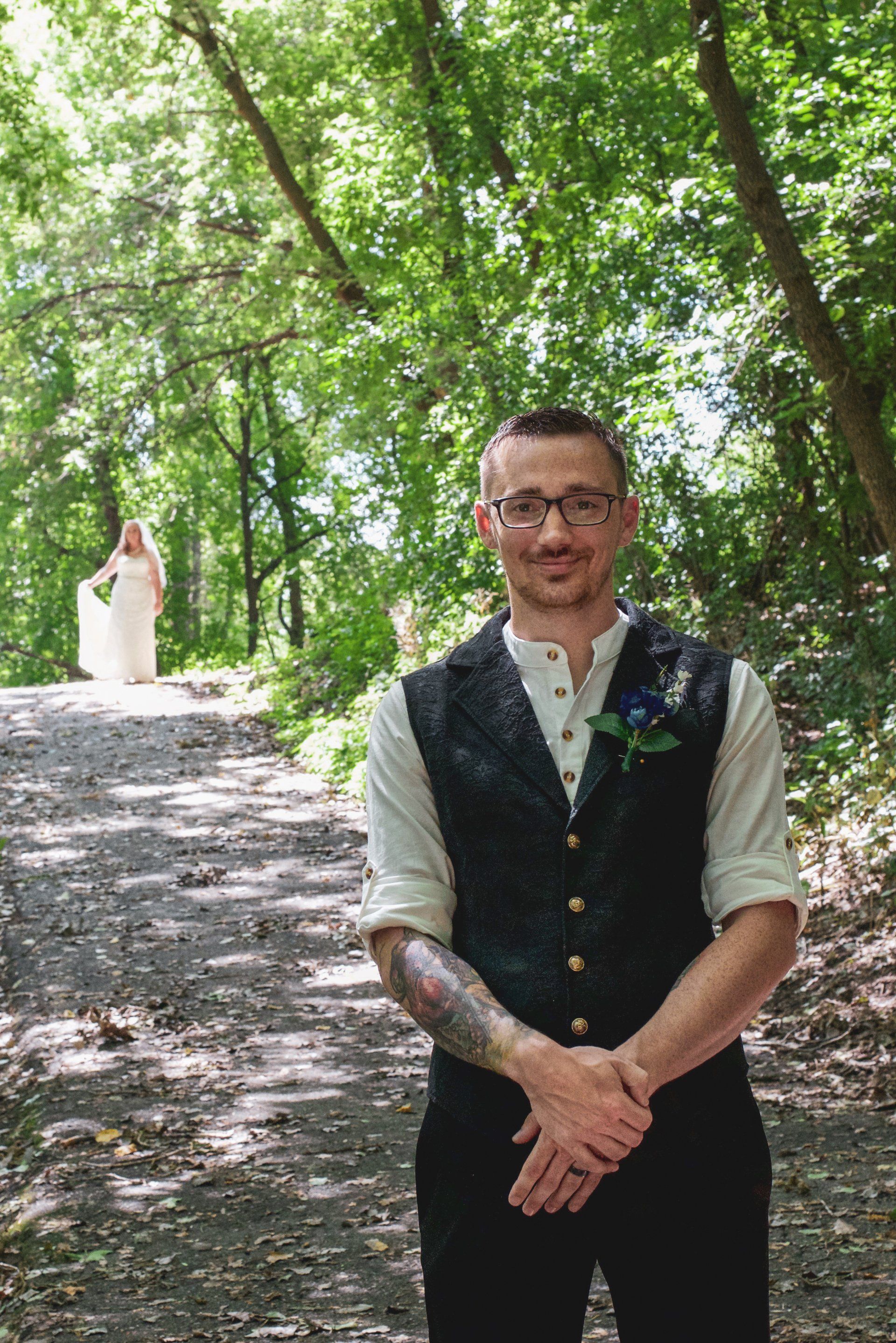A man with a tattoo on his arm stands in front of a bride in a white dress
