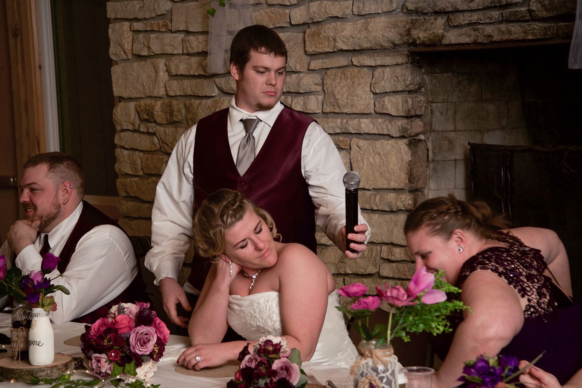 A man in a burgundy vest is giving a speech at a wedding