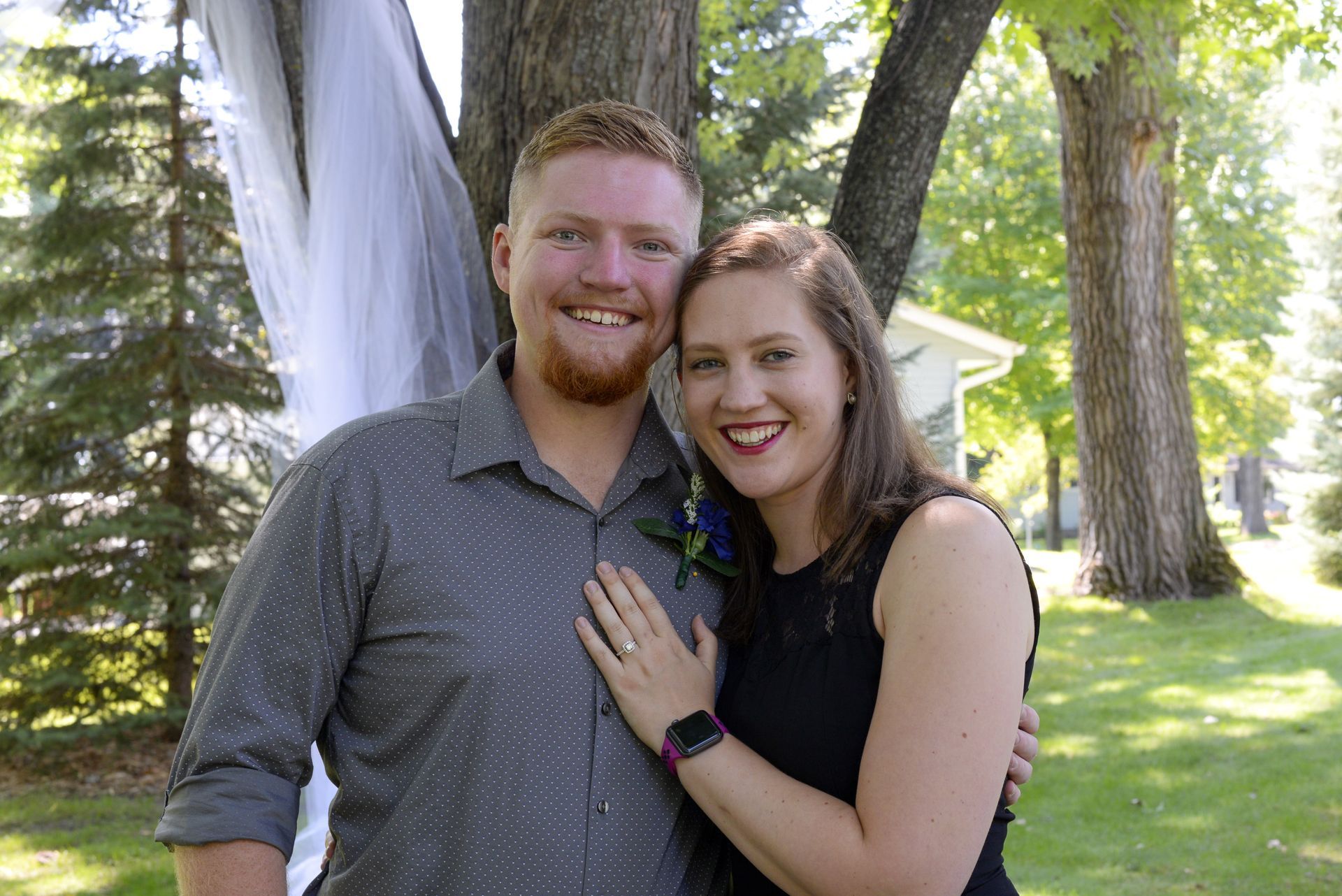 A man and a woman are posing for a picture in front of trees