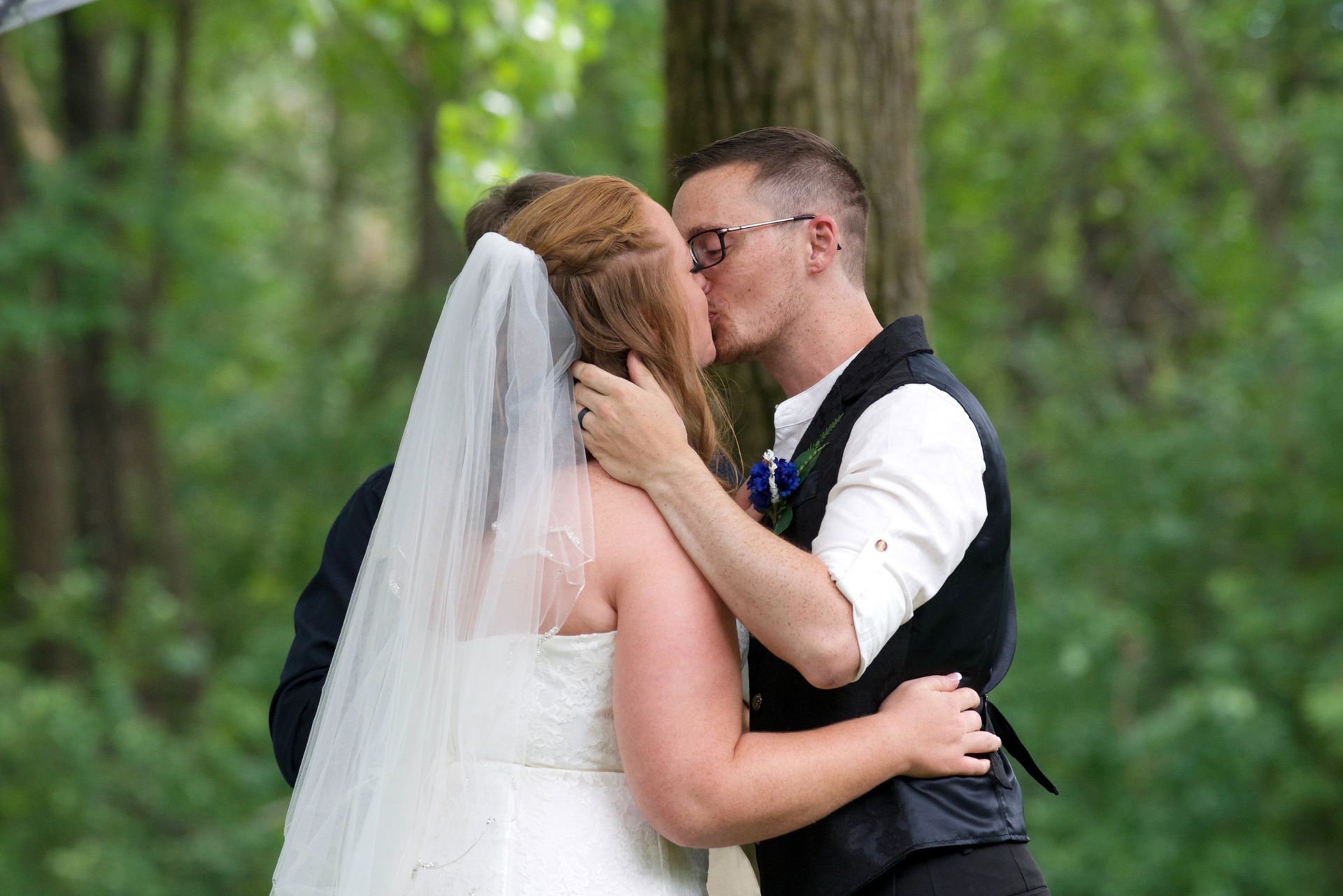 A bride and groom kissing under a tree in the woods