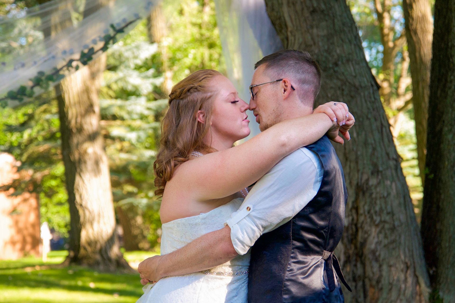 A bride and groom are kissing under a veil in the woods
