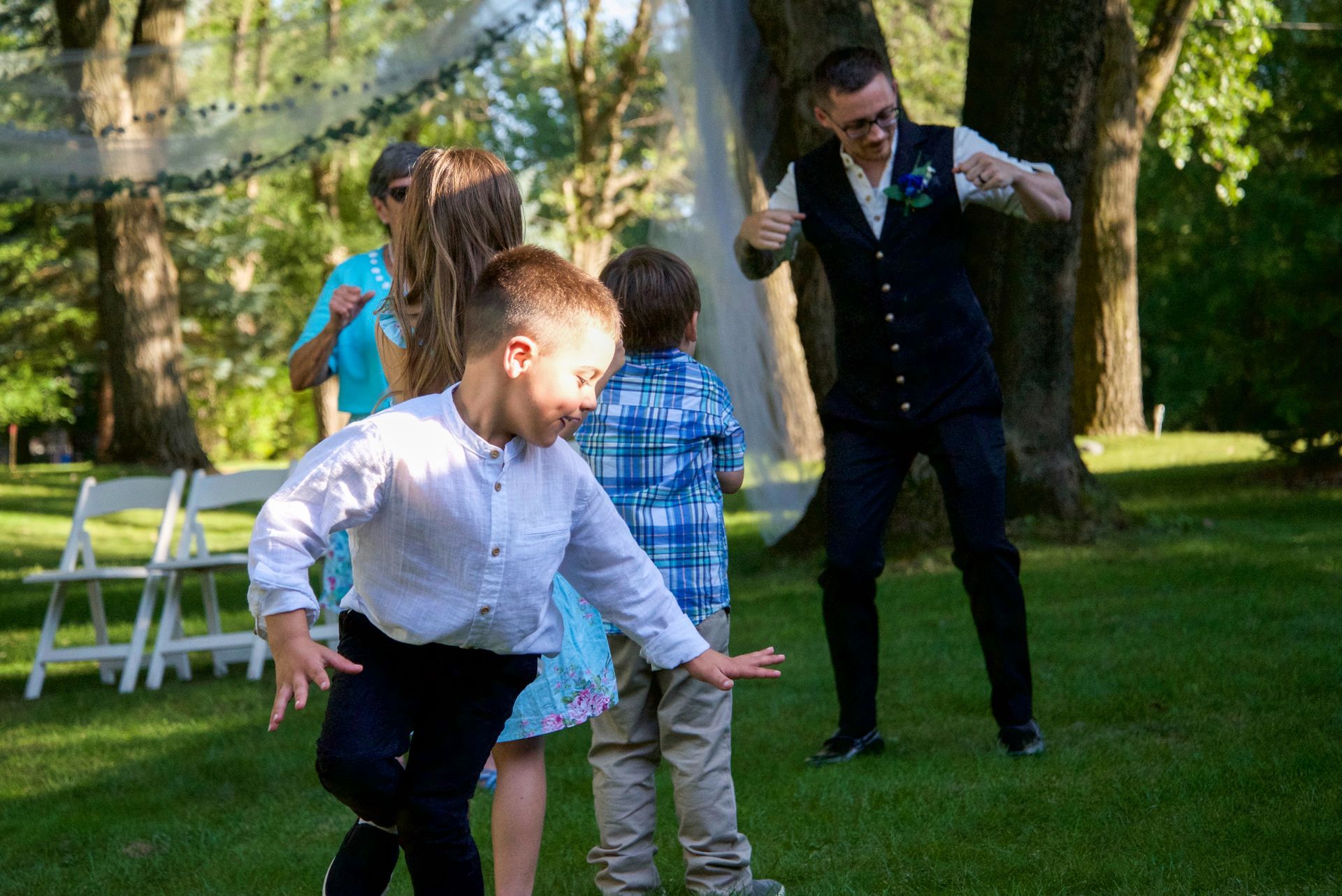A group of children are playing in the grass with a man dancing in the background