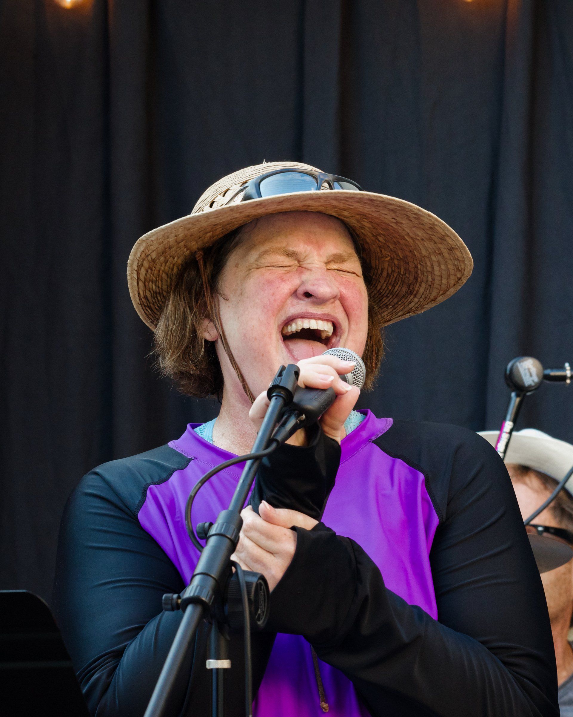 A woman wearing a straw hat is singing into a microphone