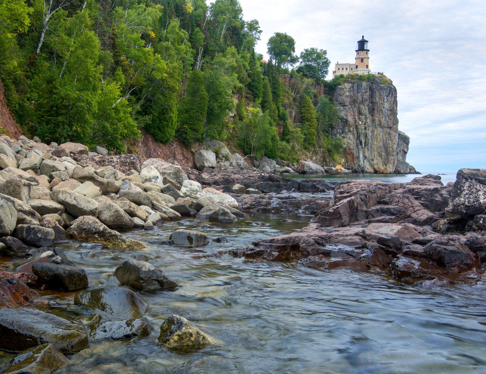 A lighthouse sits on top of a rocky cliff overlooking a body of water