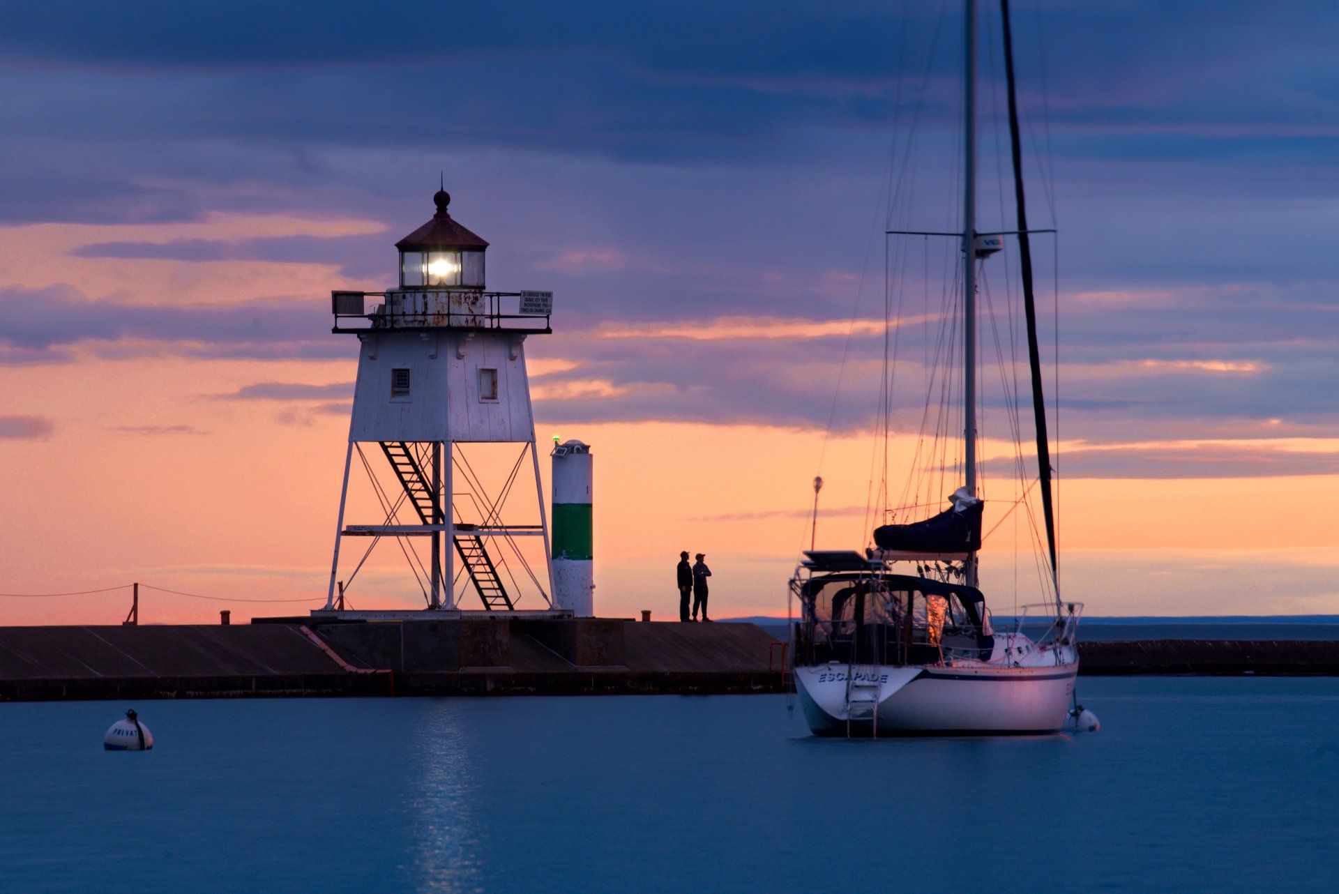 A lighthouse and a sailboat in the water at sunset