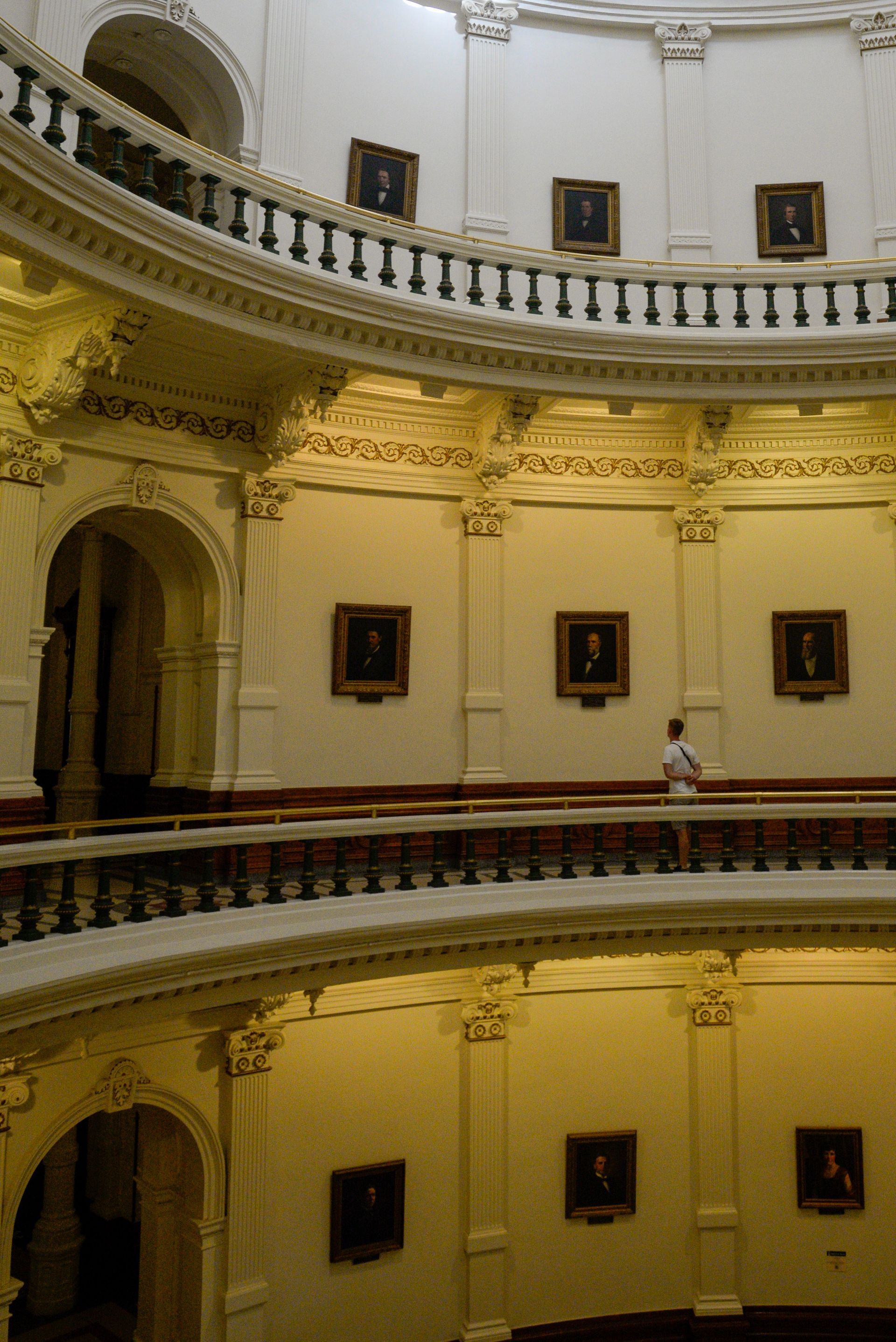 A man stands on a balcony in a building with portraits on the walls