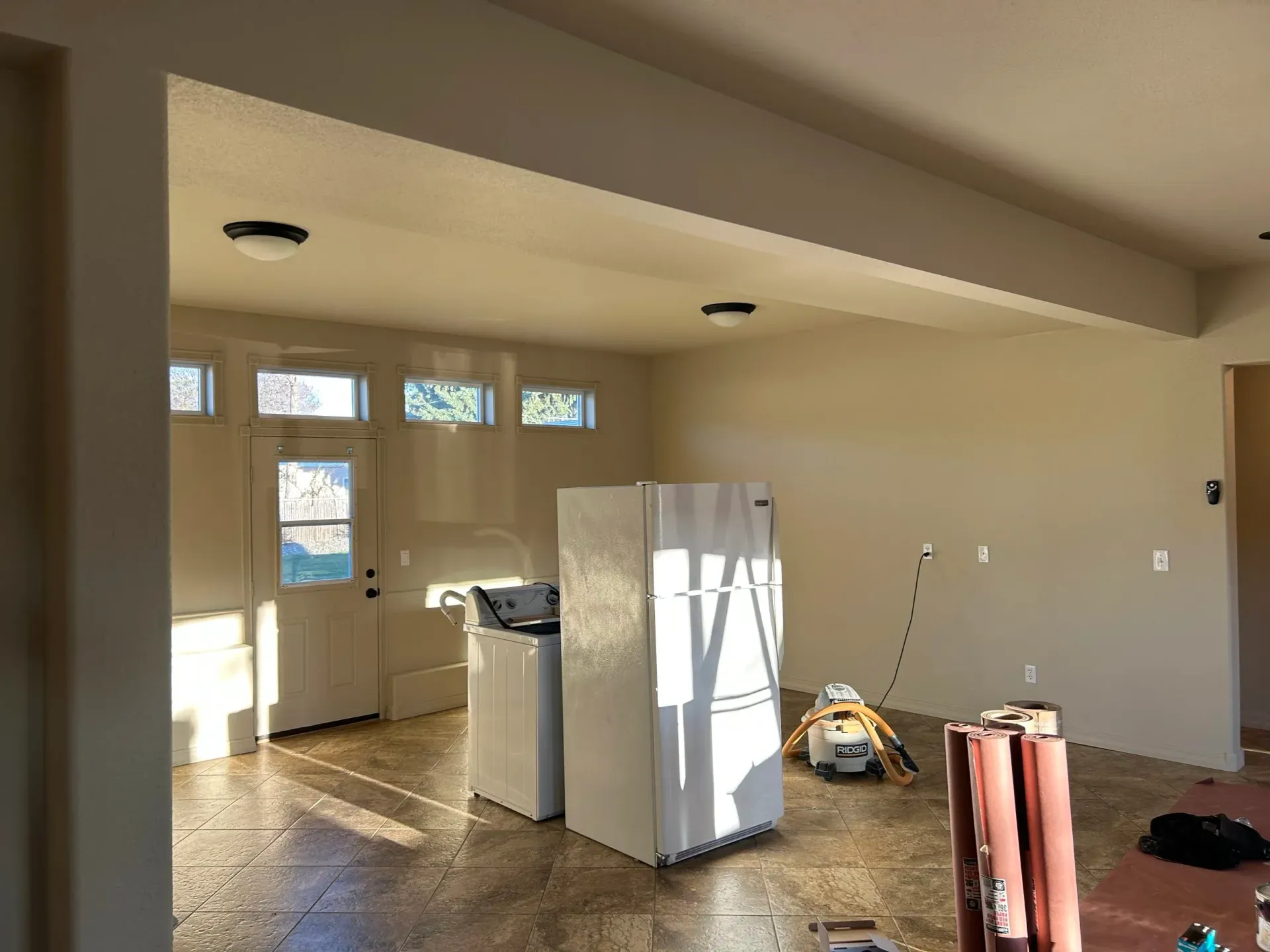 Interior view of a kitchen under renovation, with a refrigerator, washing machine, and bare concrete floor.