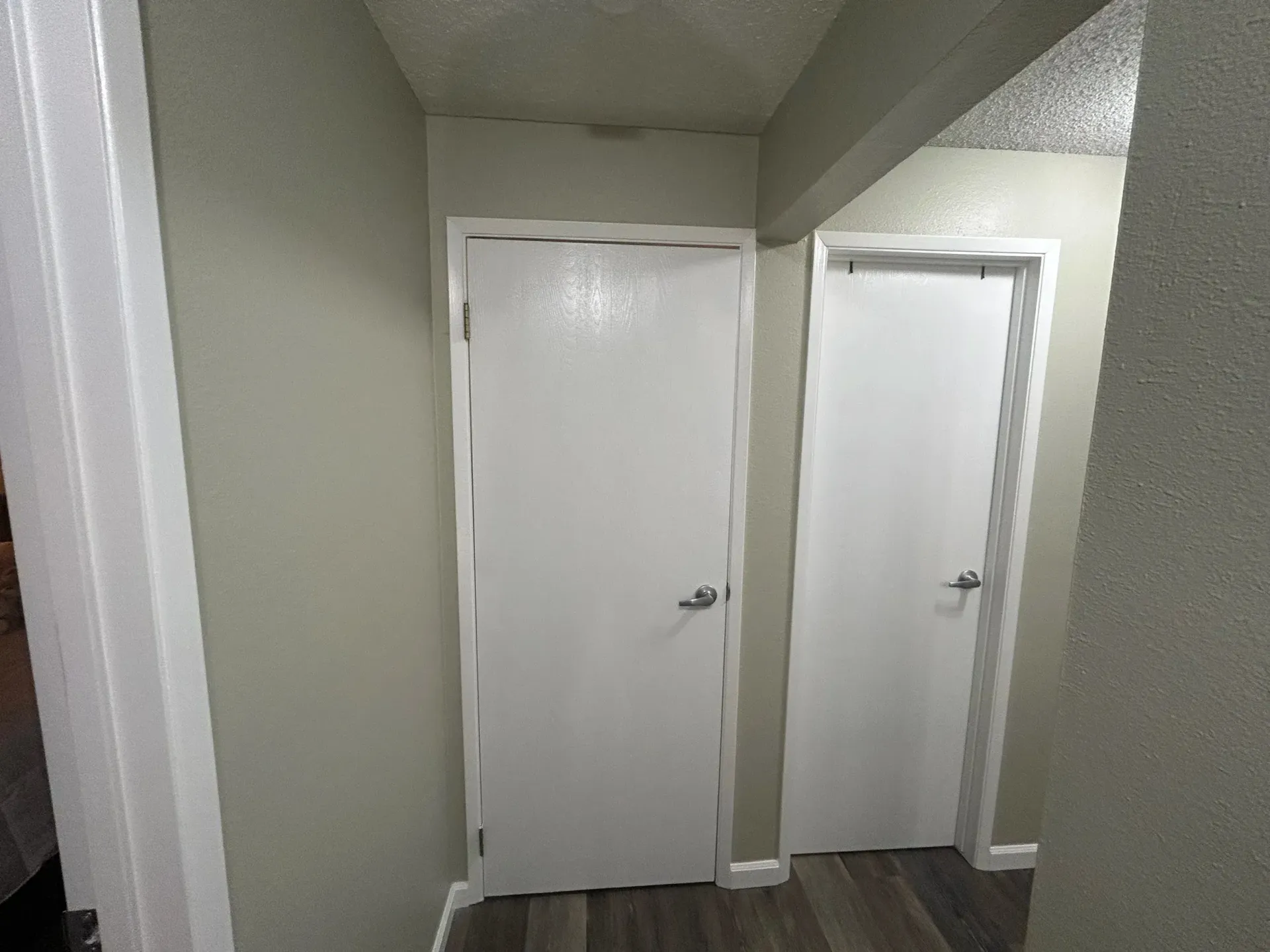 Two white doors in a hallway with gray walls and wood-look flooring.