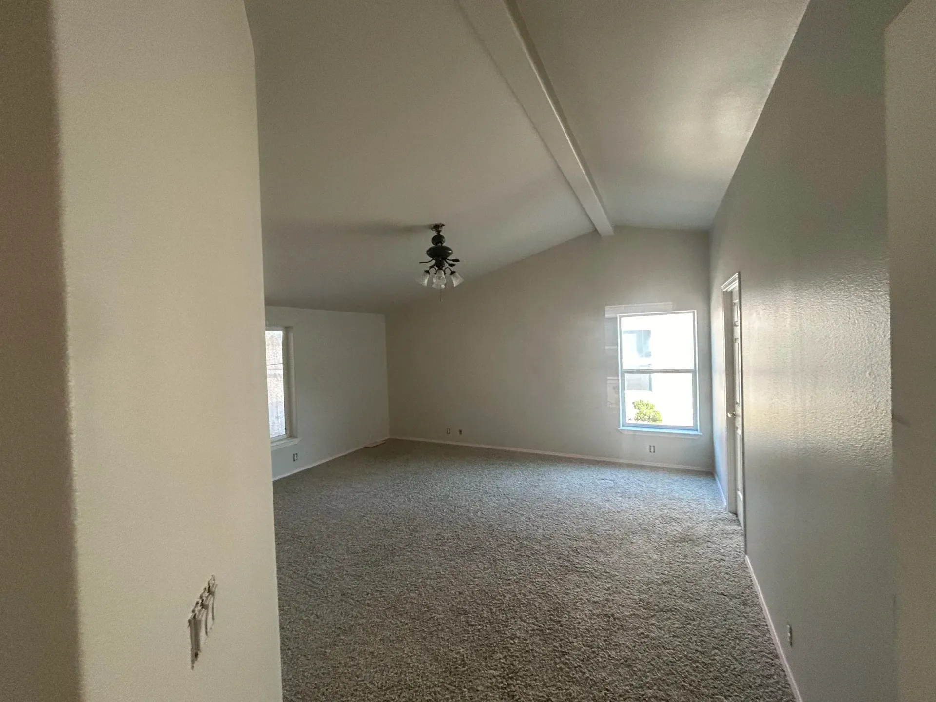 Empty room with a vaulted ceiling, textured walls, and a patterned carpet.