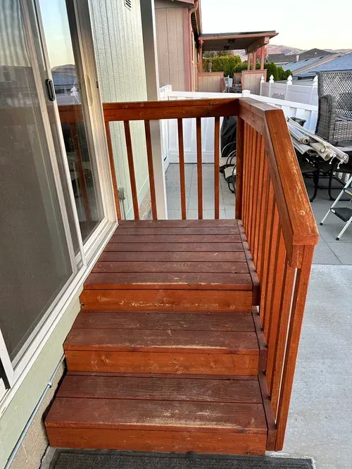 Wooden outdoor stairs with a railing next to a sliding glass door and a cement patio.