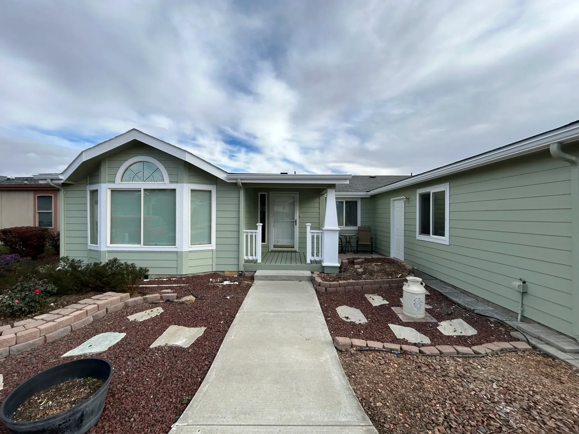 Light green house with a concrete walkway and landscaping under a cloudy sky.