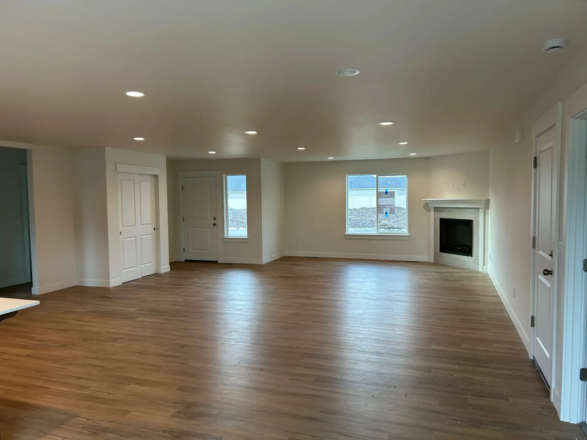 Empty living room with wood flooring, white walls, recessed lighting, and a fireplace.