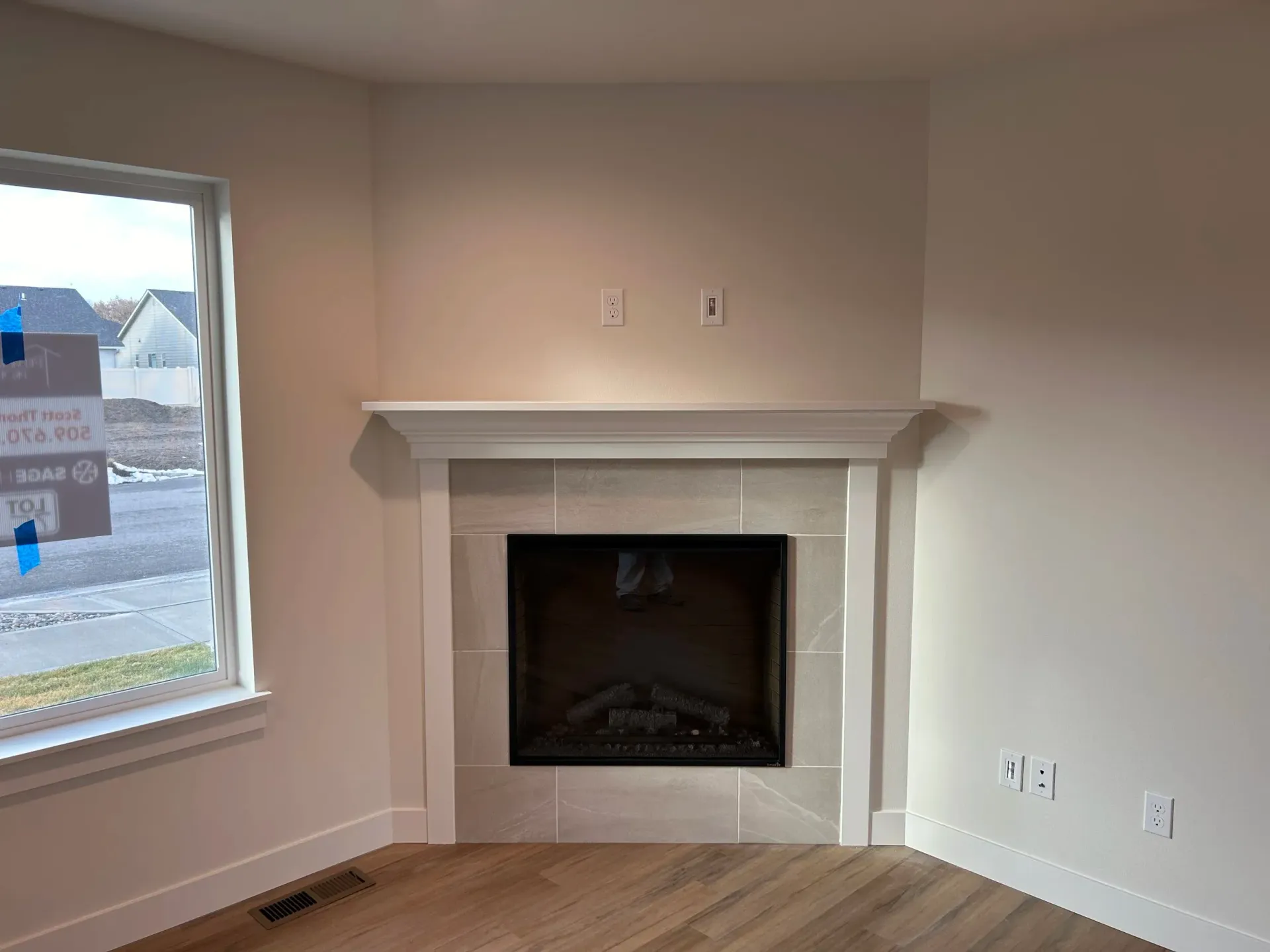 Corner fireplace with white mantle, tile surround, and built-in screen; next to window.