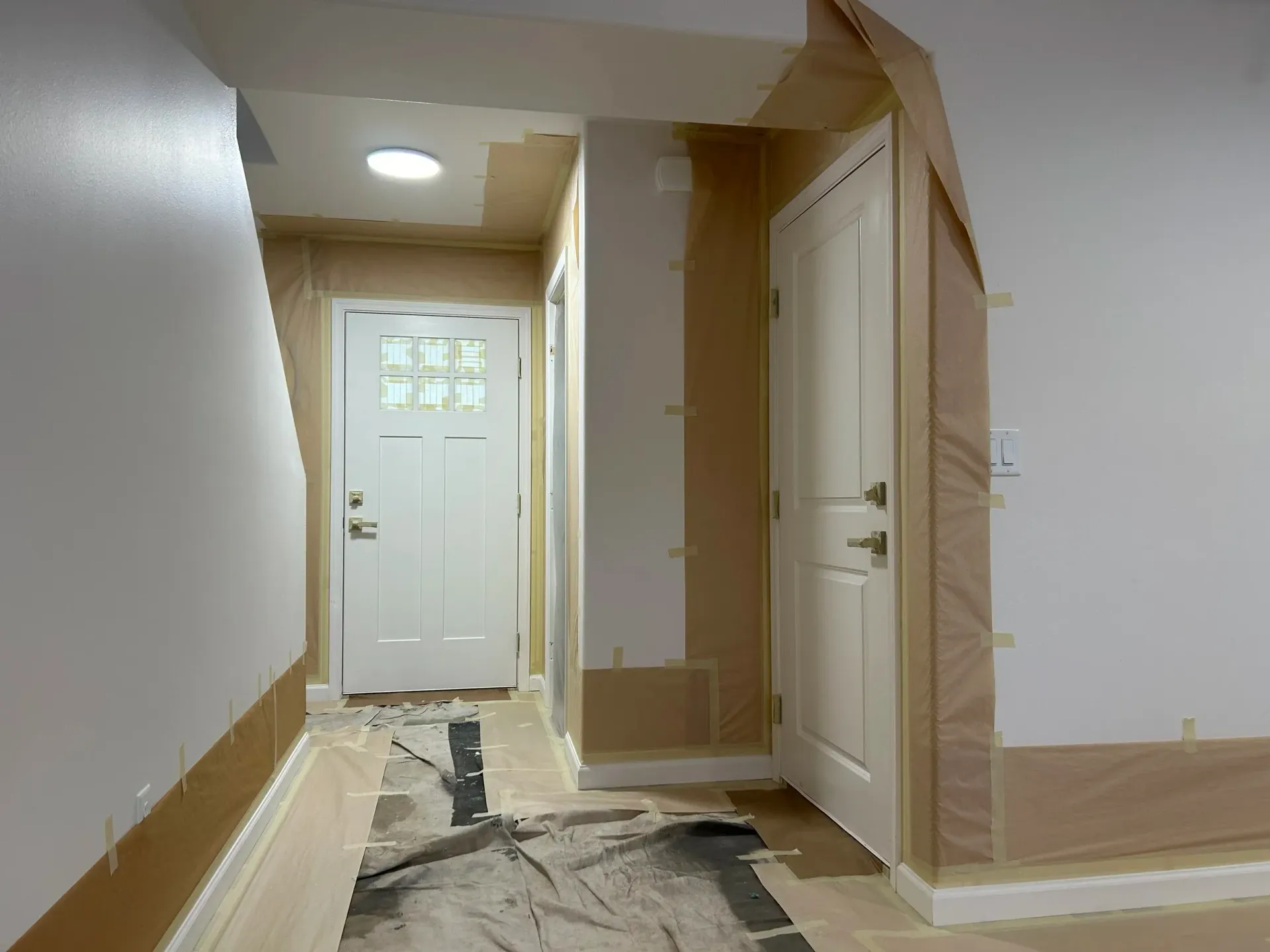 Hallway with two white doors, freshly painted walls, and protective paper.