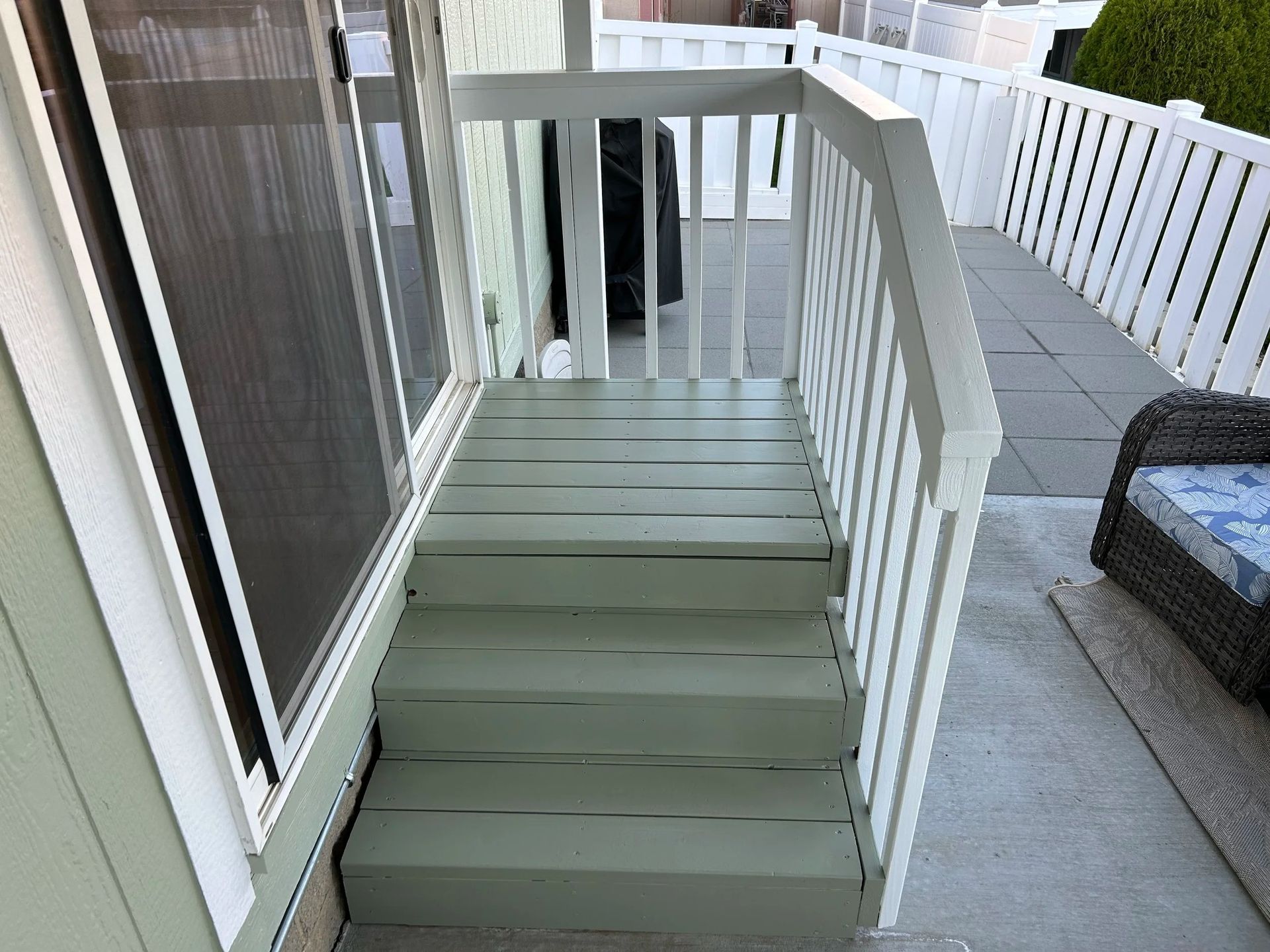 Green painted wooden steps leading down from a deck, with a white railing.