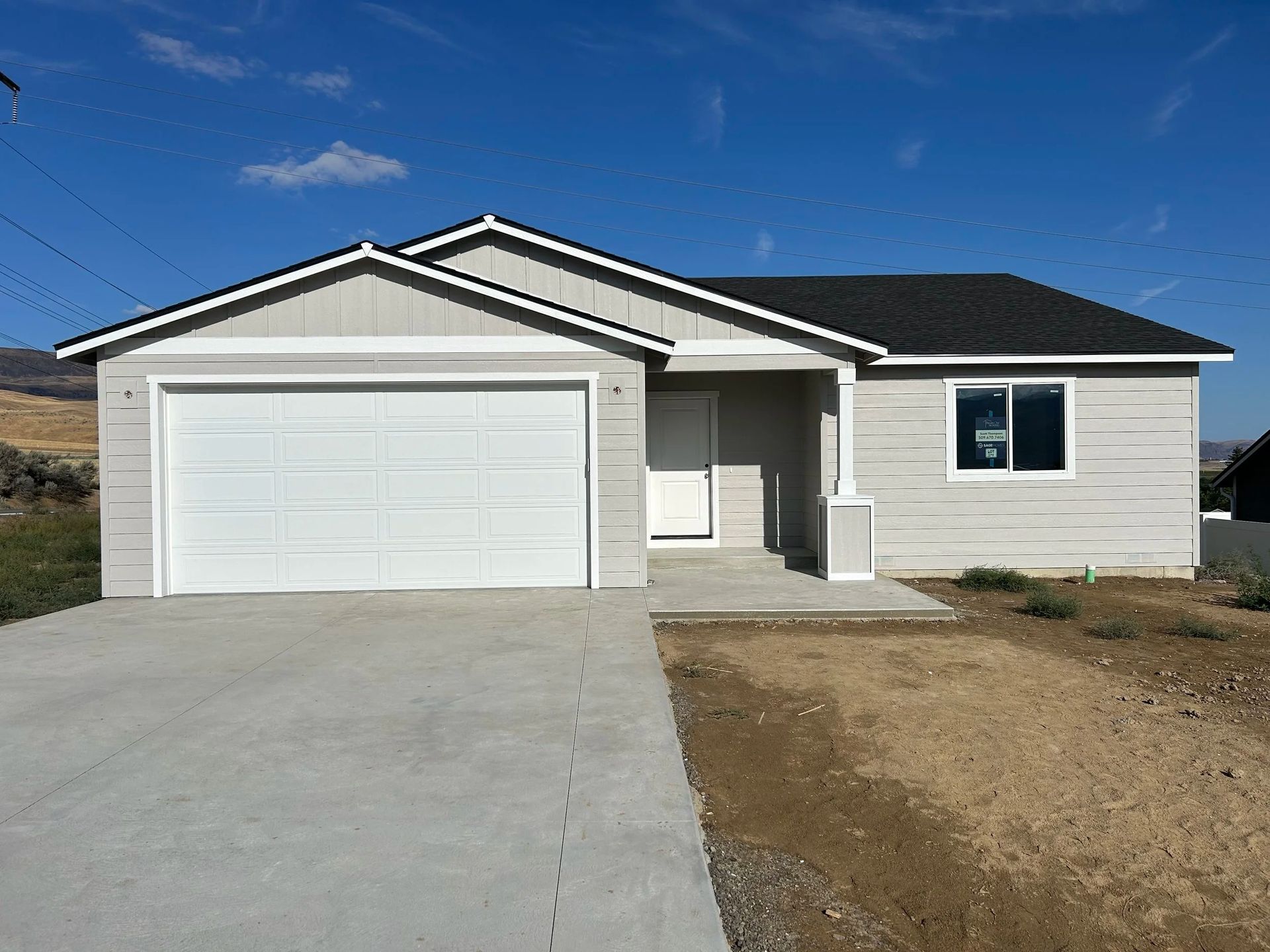 Light gray ranch house with a white garage door on a concrete driveway, set against a blue sky.