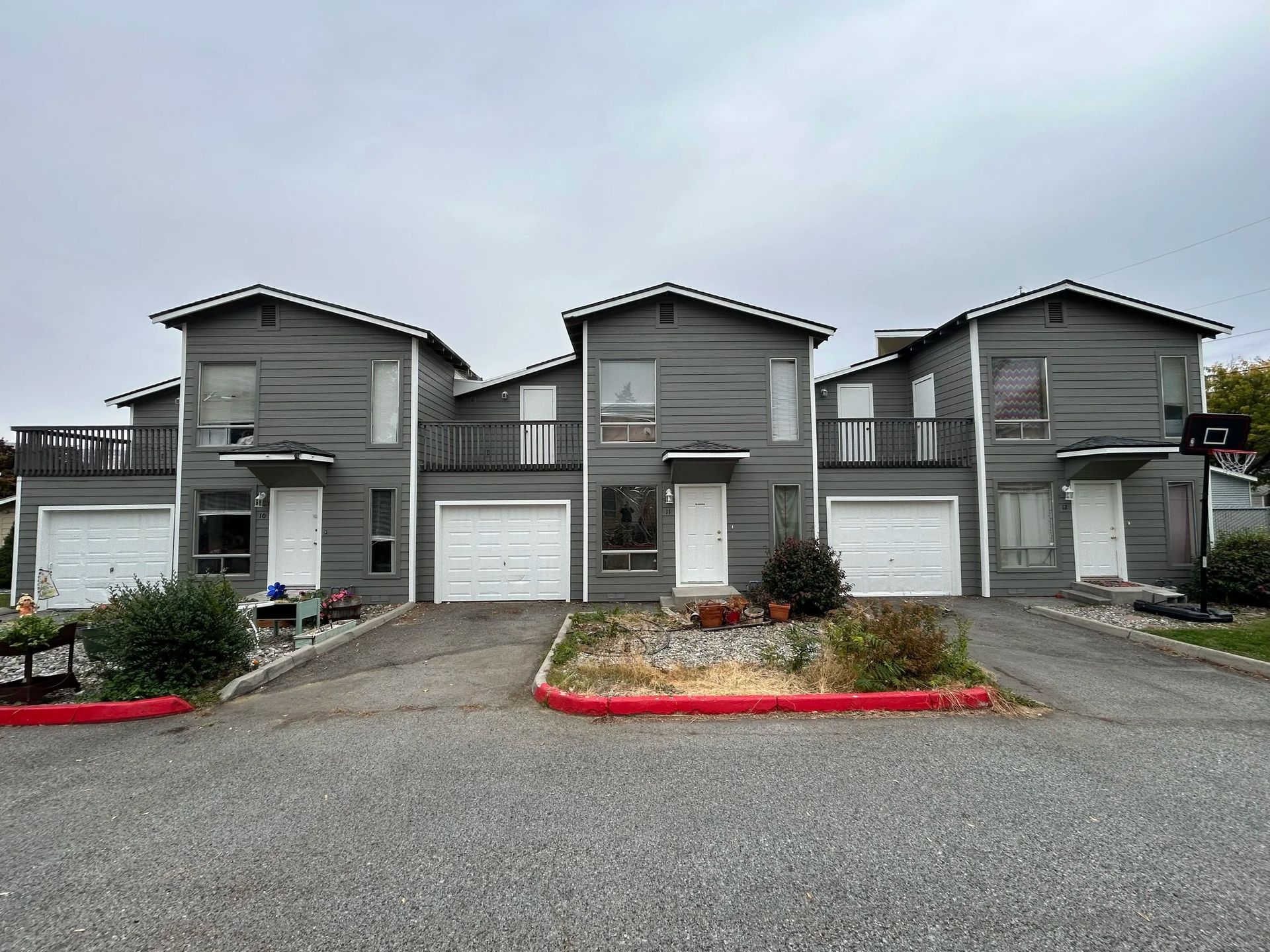 Three two-story gray townhouses with white garage doors under an overcast sky.