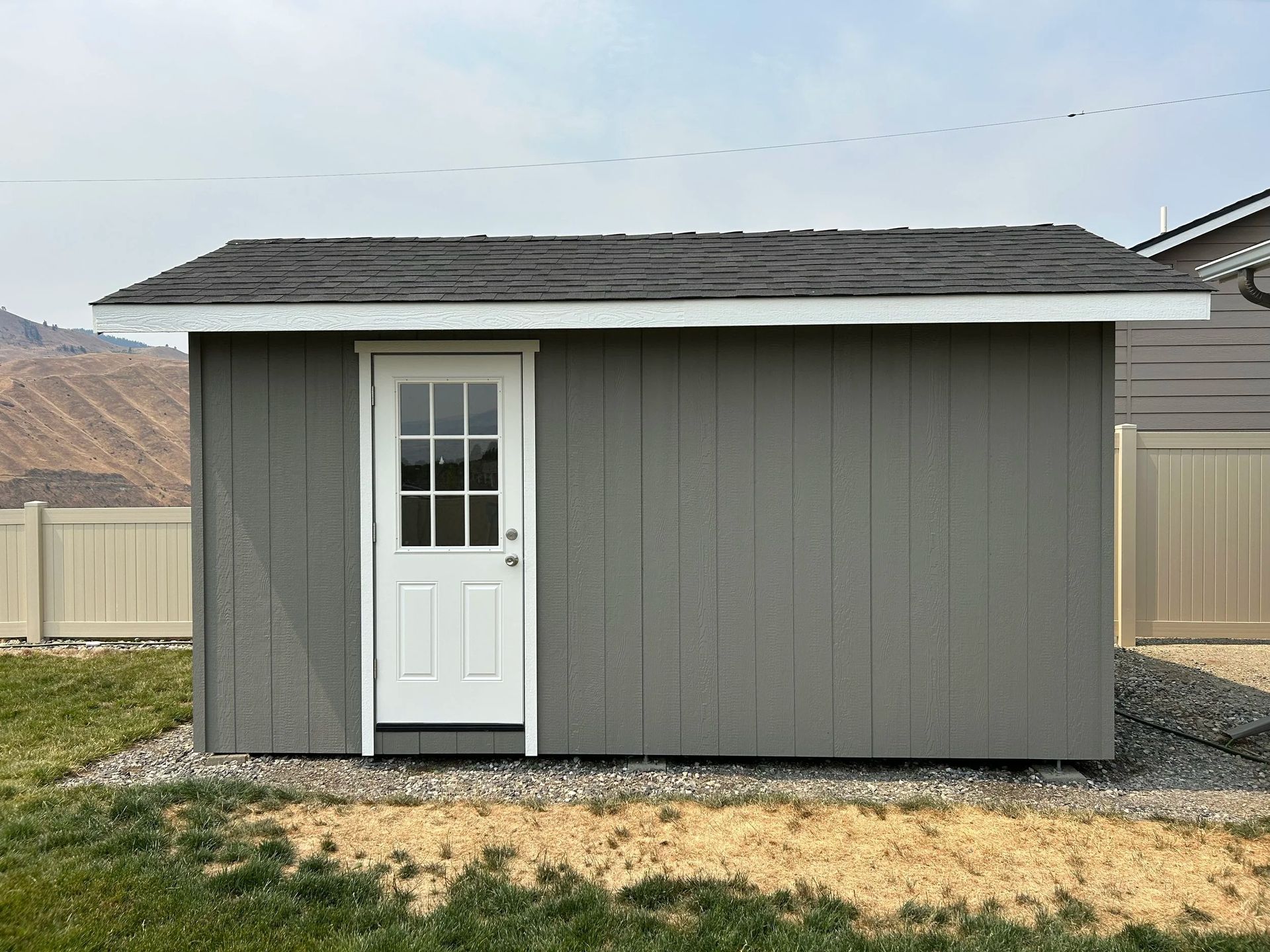 Gray shed with white door, black roof, and light green grass.