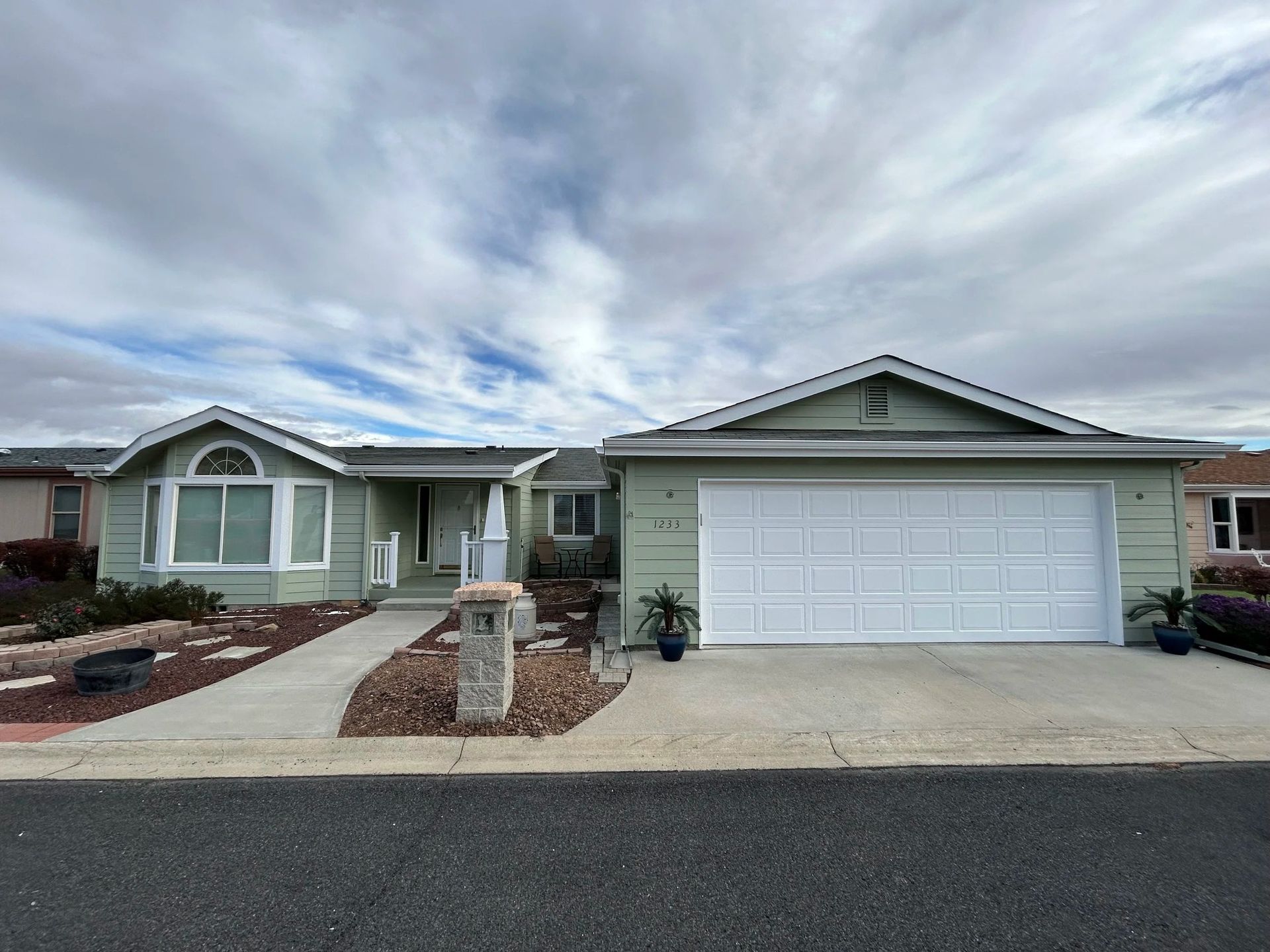 Green house with white garage door and walkway, blue sky.