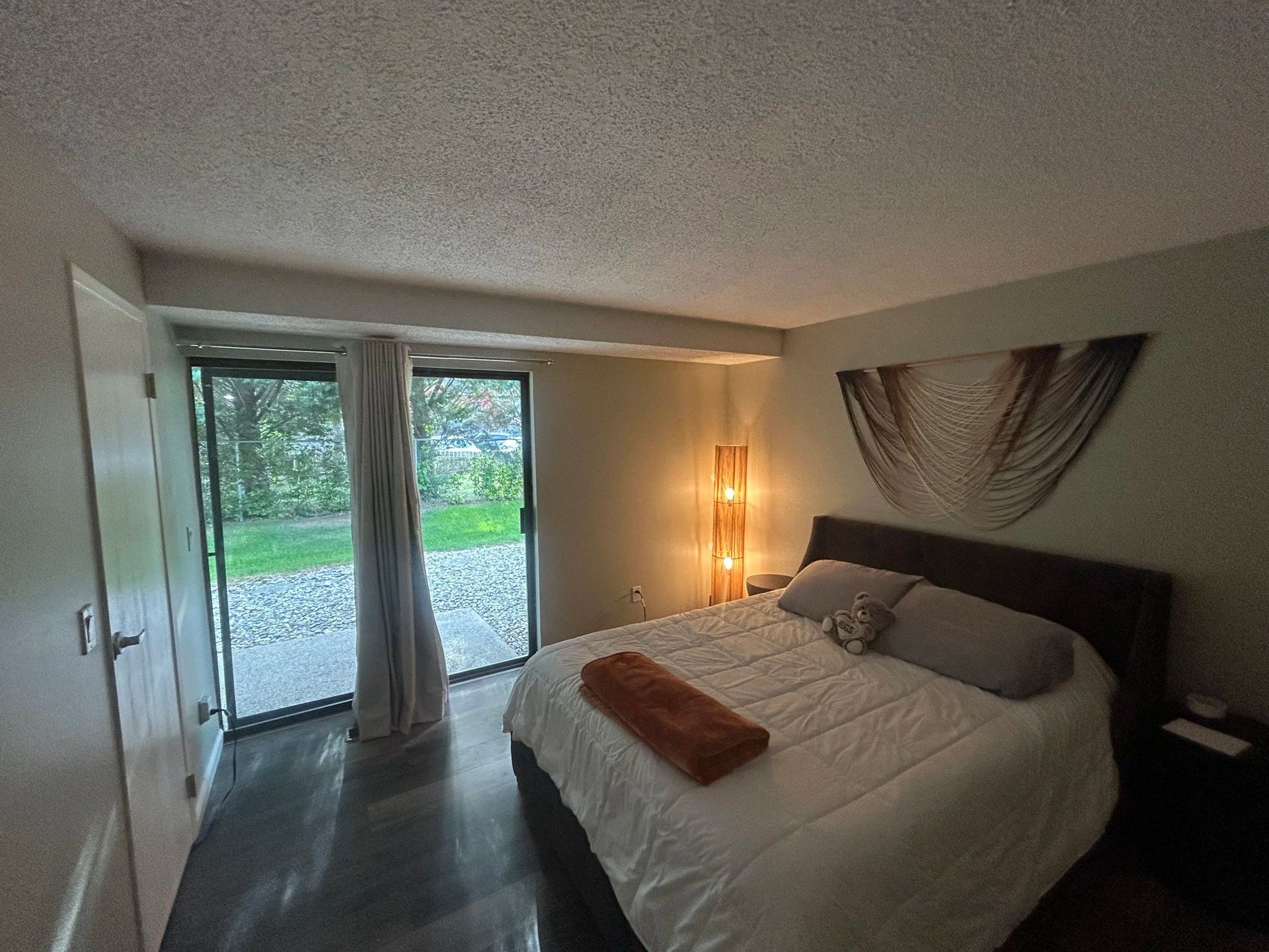 Bedroom with a bed, sliding door to a patio, and a tall lamp. Neutral colors dominate.