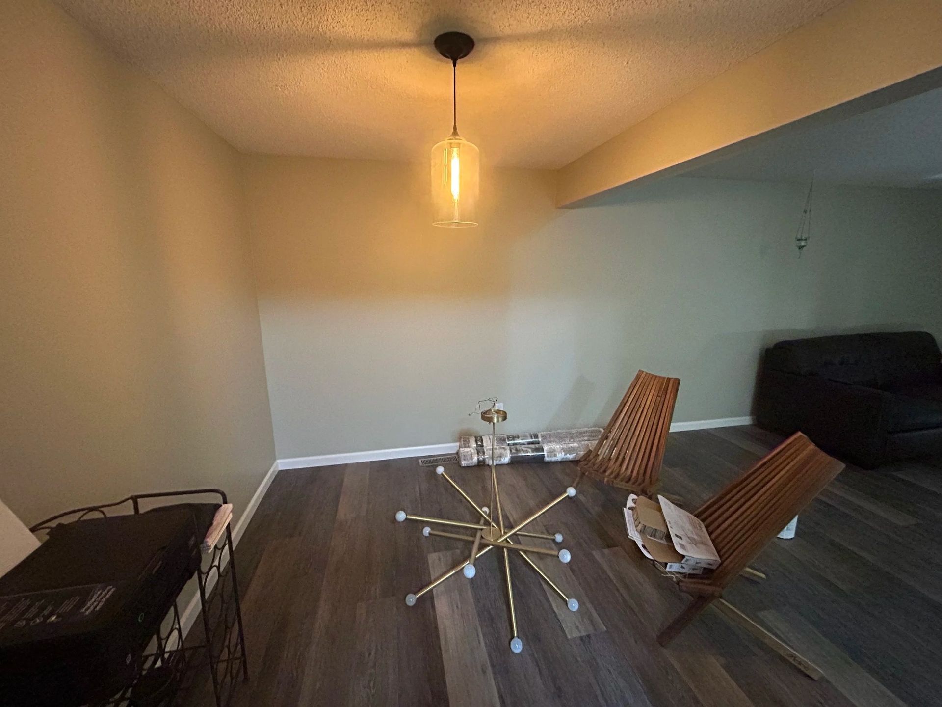 A room with wooden floors, a gold chandelier, and two wooden chairs.