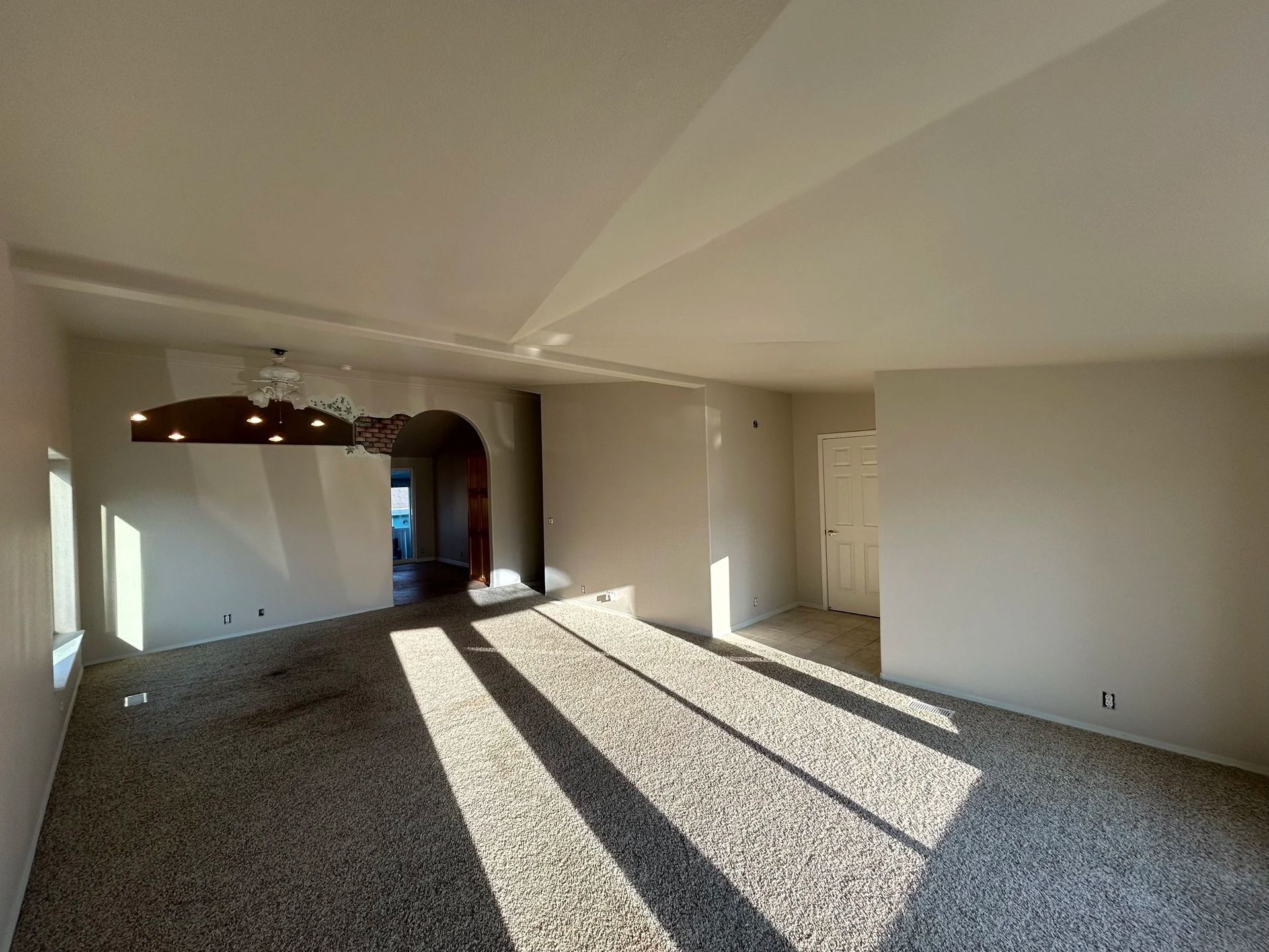 Empty room with unfinished flooring, sunlight casting long shadows across it. White walls and ceiling.