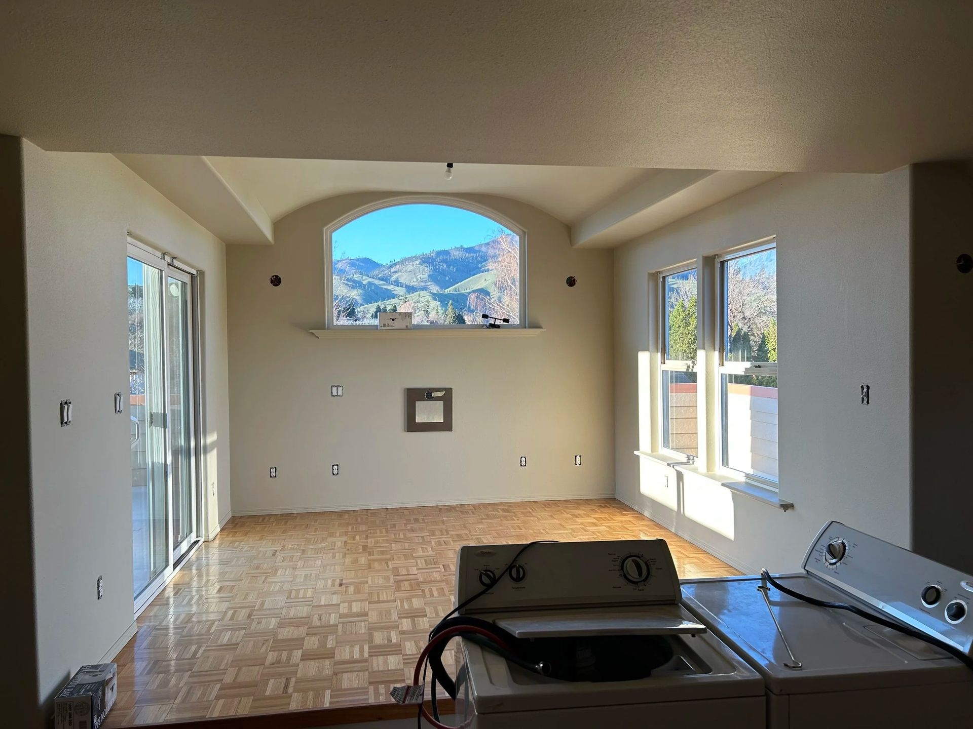 Empty room with arched window, mountain view, and washer/dryer on a wood floor.