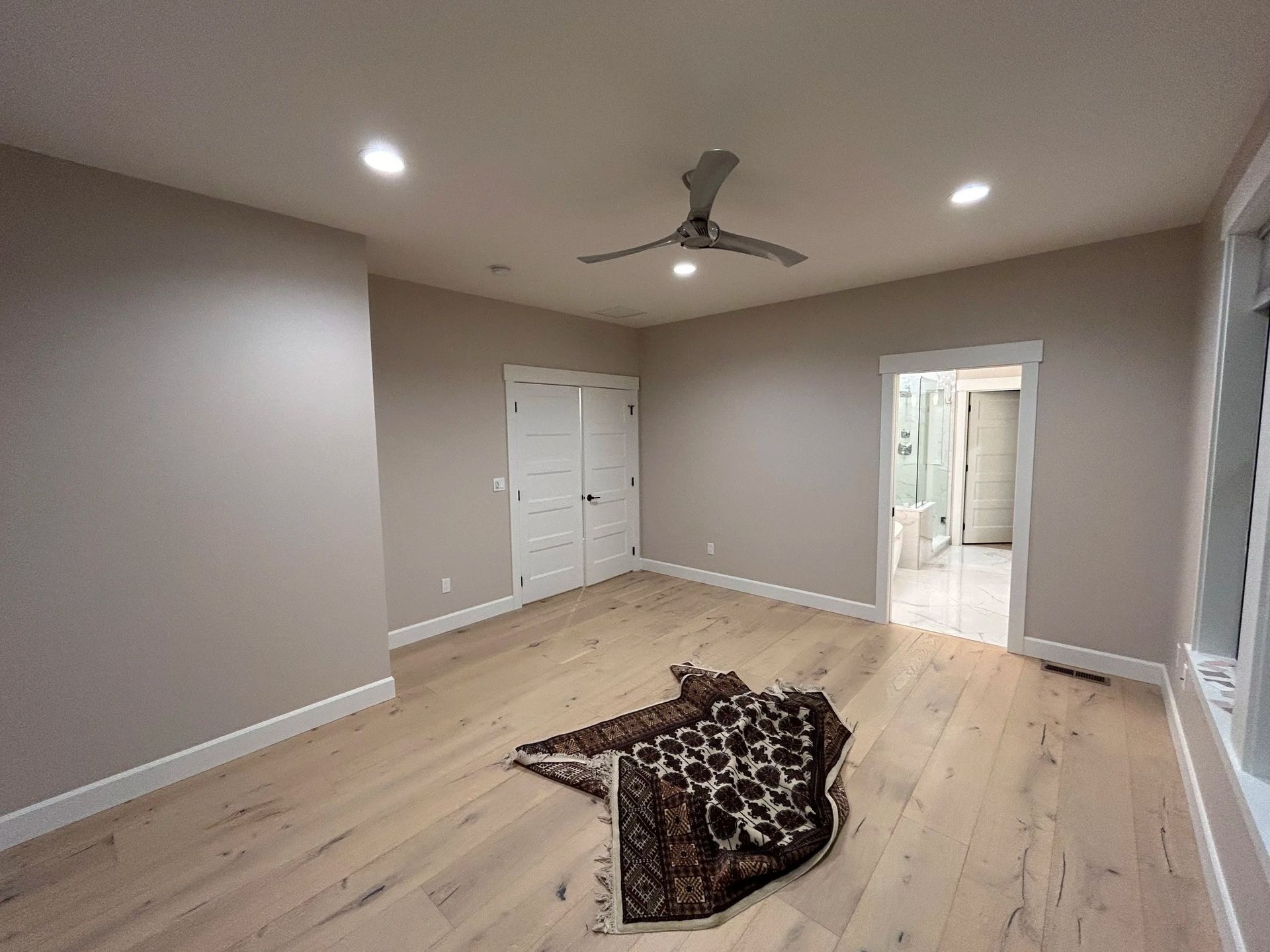 Empty bedroom with hardwood floors, a ceiling fan, and a rug.