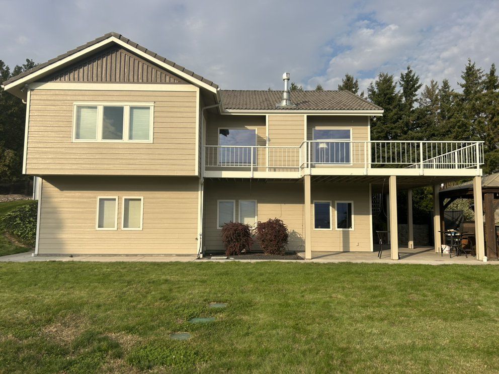 Two-story beige house with a deck overlooking a green lawn.