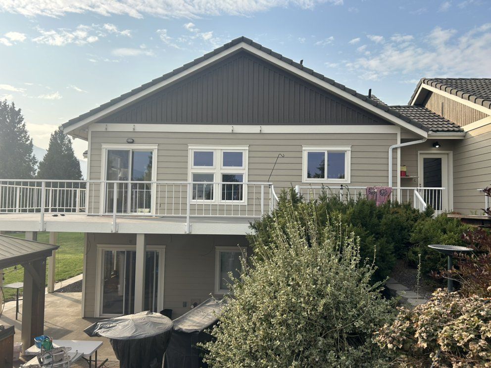 Back of a house with deck and white railings, tan siding, and green roof in a yard.