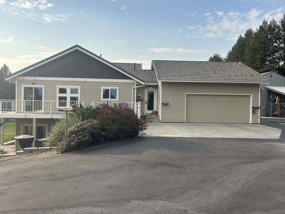 Tan house with attached garage, deck, and blacktop driveway under a blue sky.