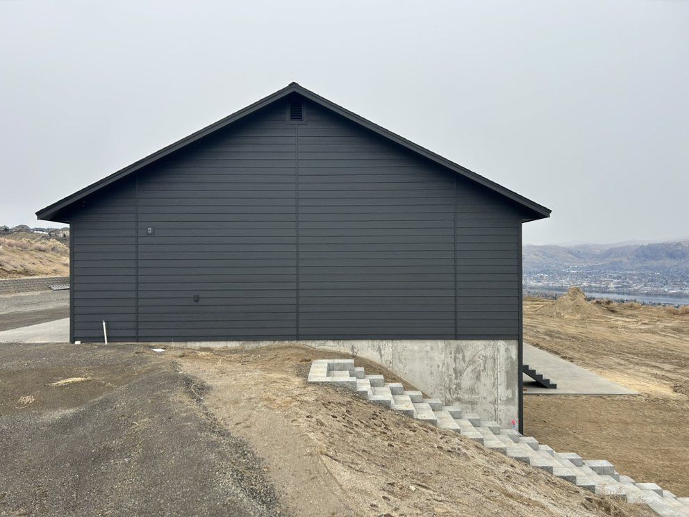 Dark gray building with a gabled roof on a concrete base, steps leading to a door.