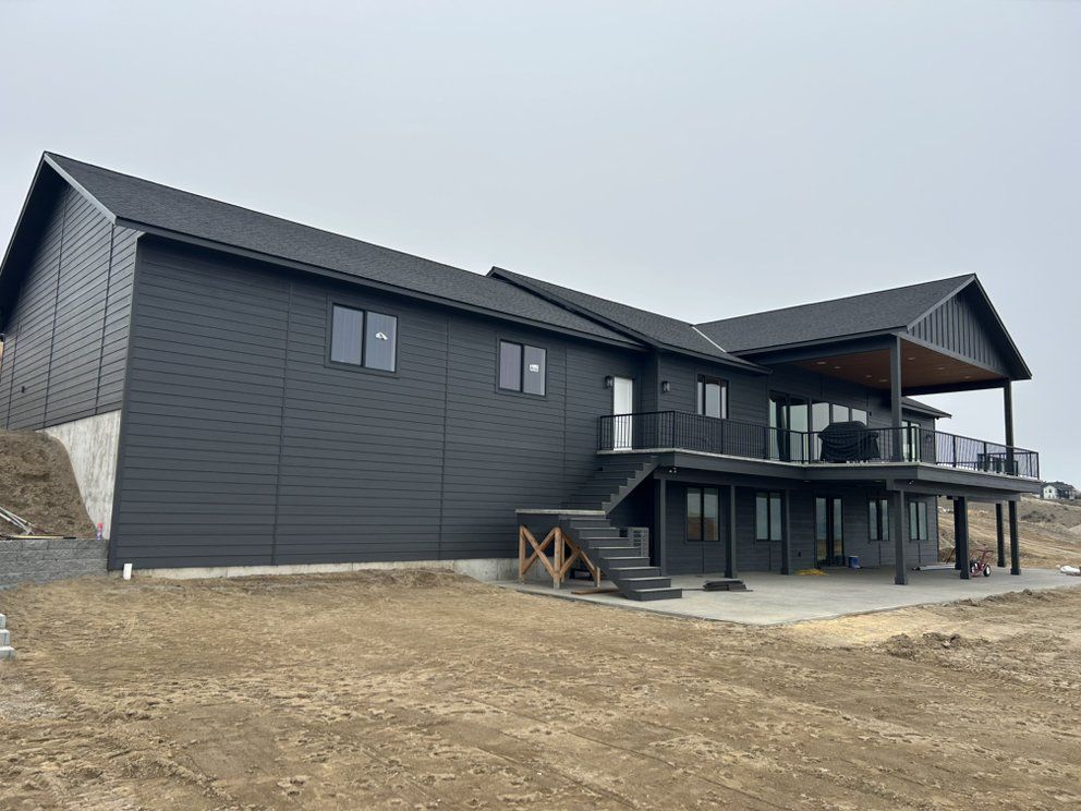 Black modern house with deck and stairs on a cloudy day.