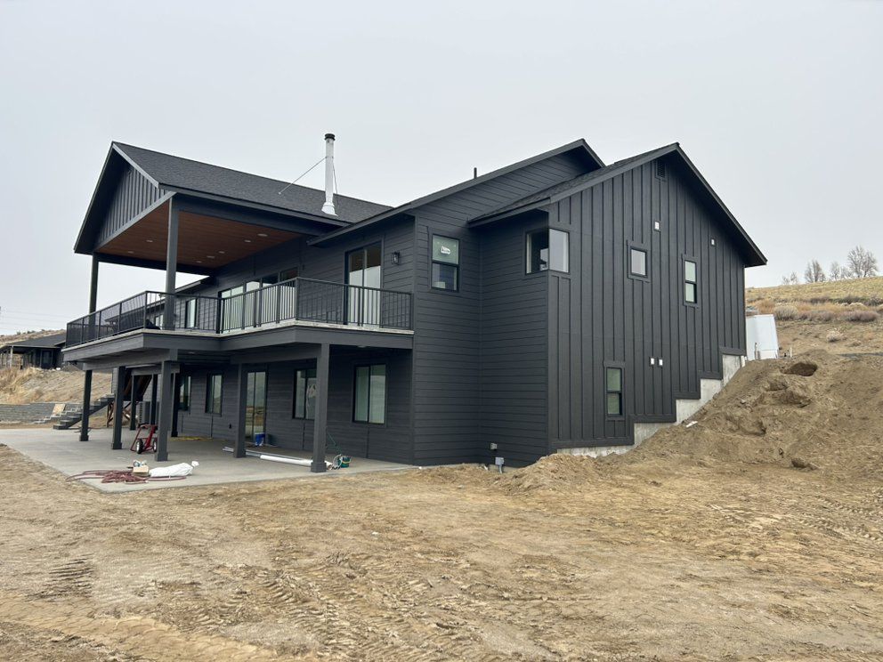Black modern house with deck and stairs on a hillside, unfinished landscaping.