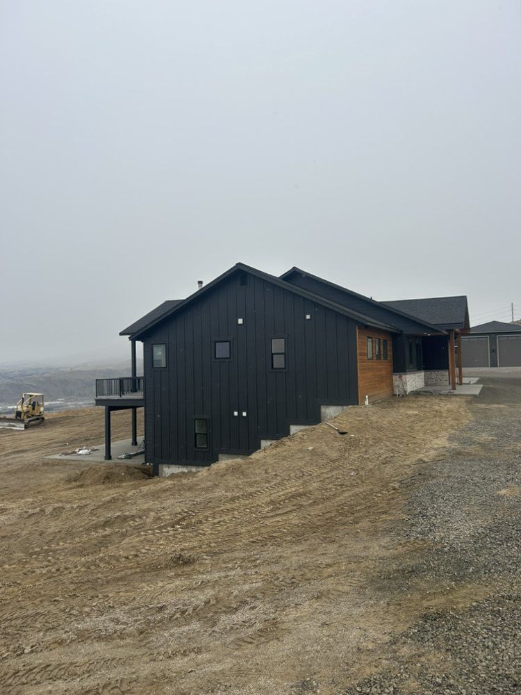 Black modern house with wooden accents on a gravel lot under an overcast sky.