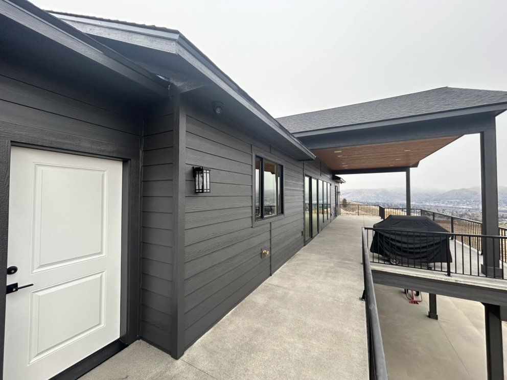 Dark gray house with white door, black trim, and covered patio overlooking a cityscape.