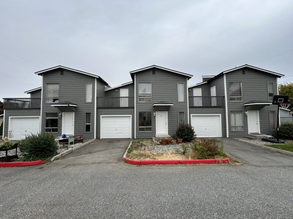 Gray townhouses with white garage doors and a red curb. Overcast sky.