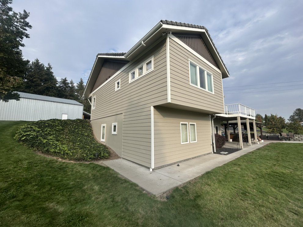 Two-story house with tan siding, white trim, and a small deck overlooking a lawn.