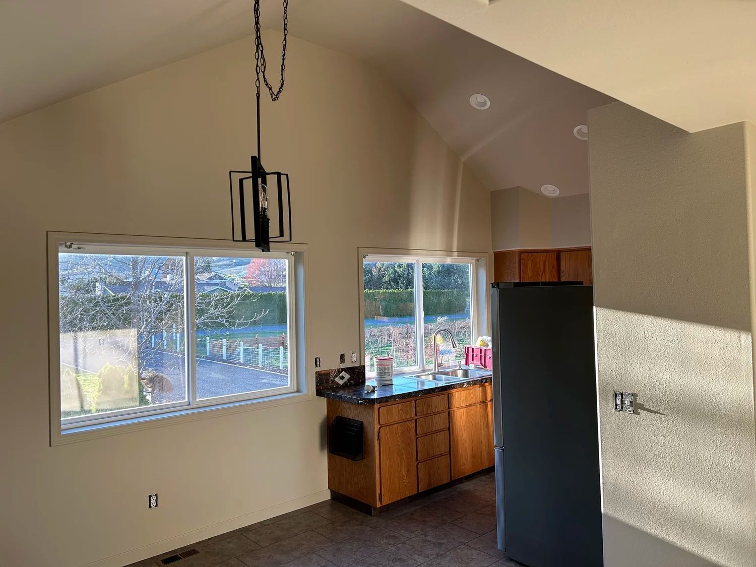 Kitchen interior with vaulted ceiling, two windows, and dark-colored cabinetry.