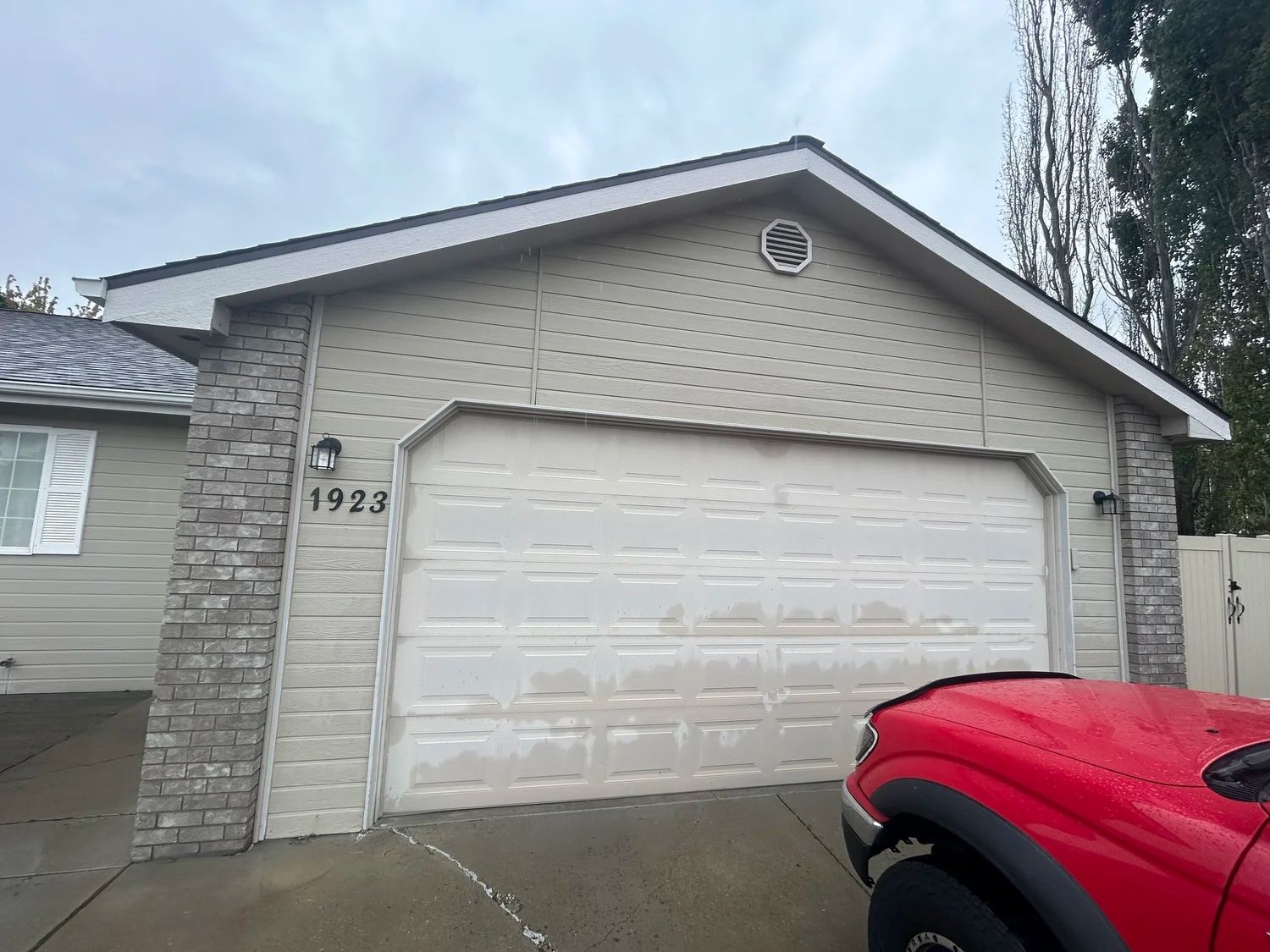 Garage with beige siding, brick accents, and a red truck parked nearby.