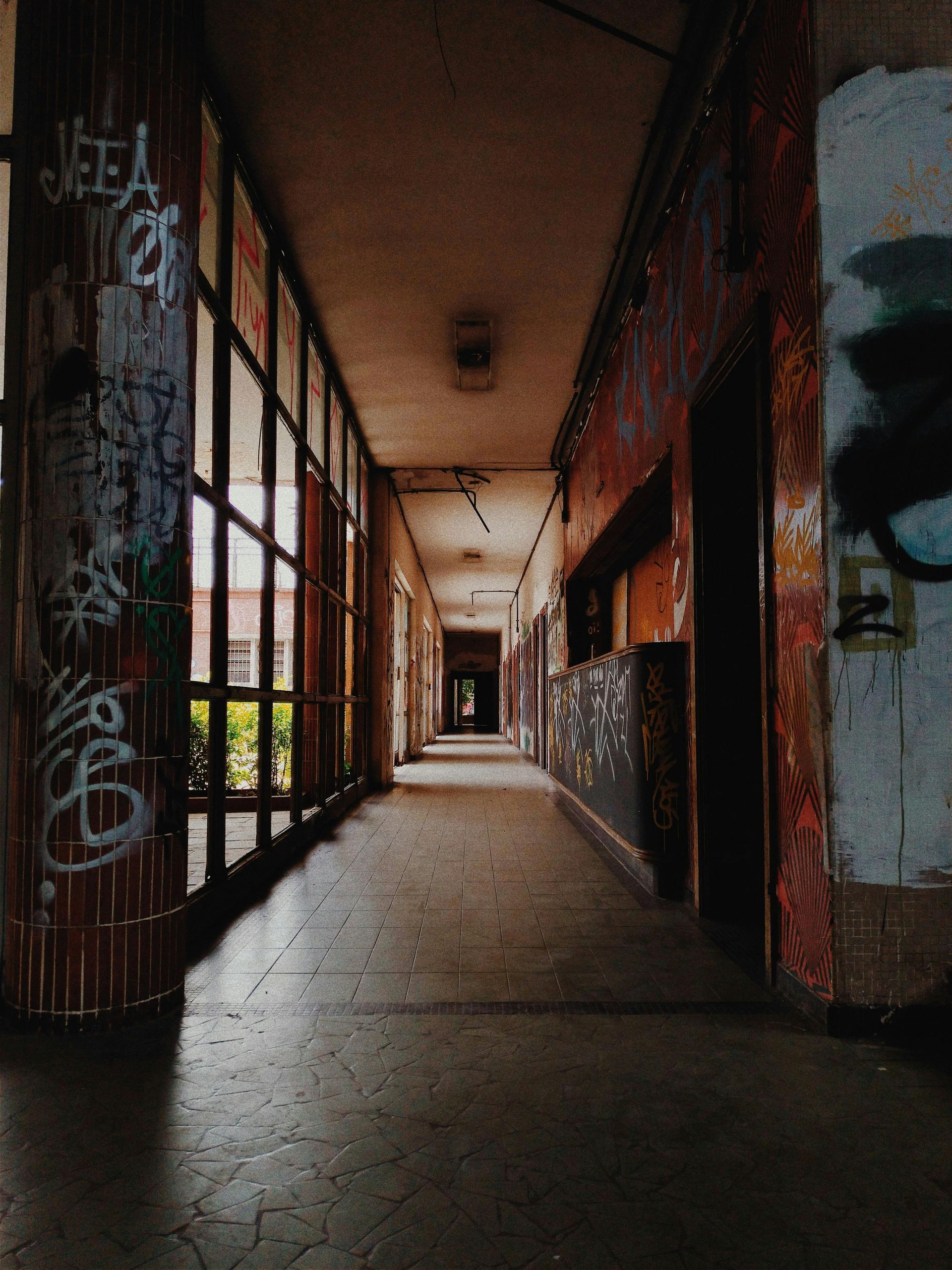 A long hallway with a lot of windows and graffiti on the walls