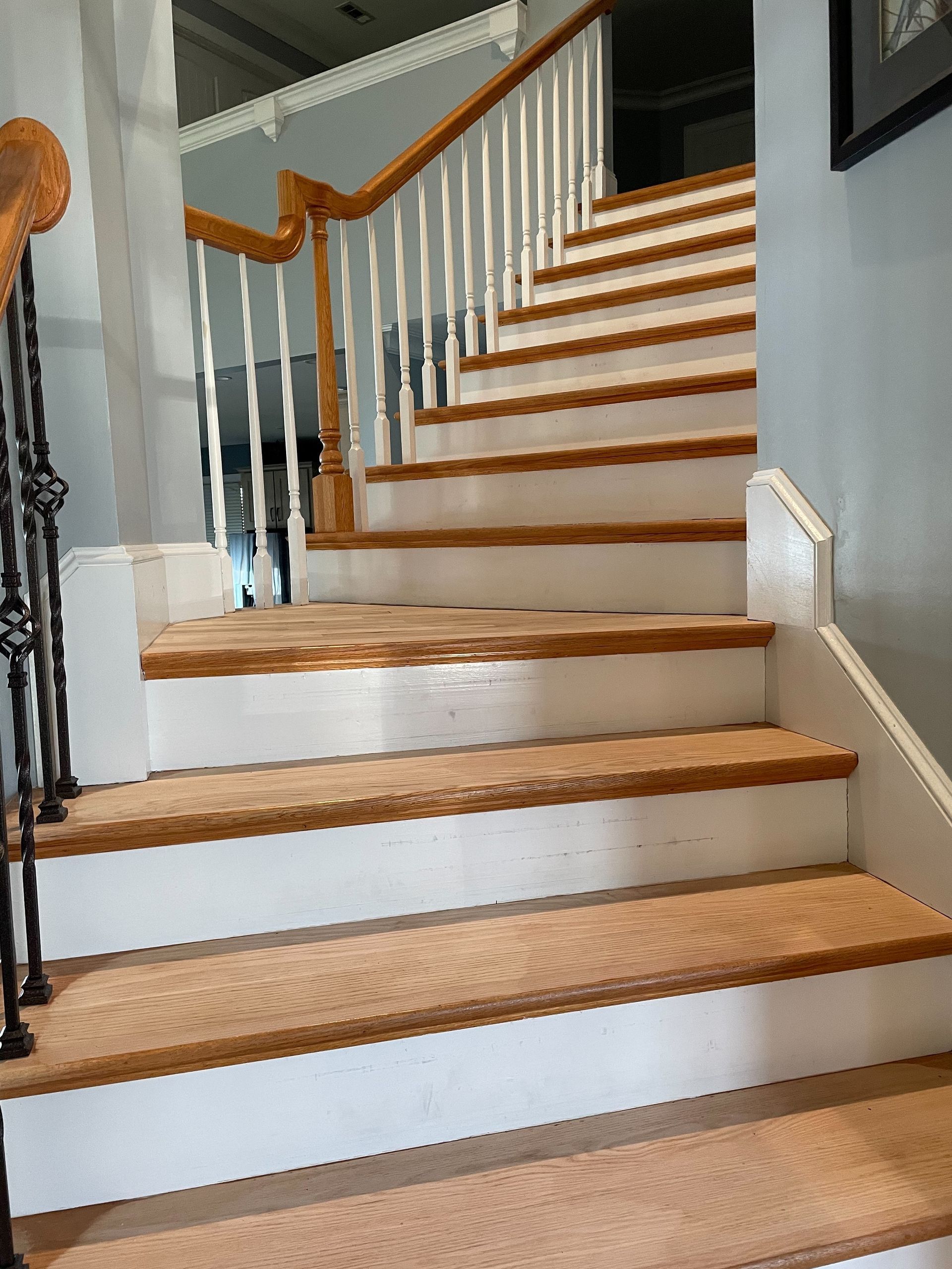 A white staircase with wooden steps and a wooden railing in a house.