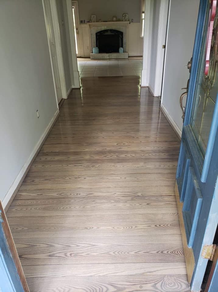 A hallway with hardwood floors and a blue door leading to a living room.