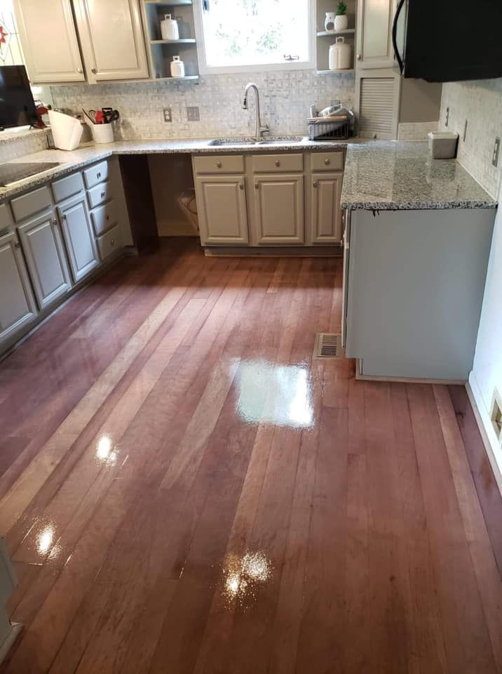 A kitchen with hardwood floors , white cabinets , granite counter tops and a sink.