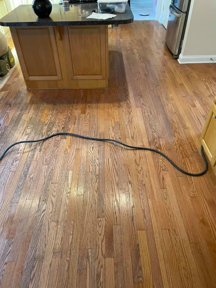 A kitchen with hardwood floors and a black cord laying on the floor.