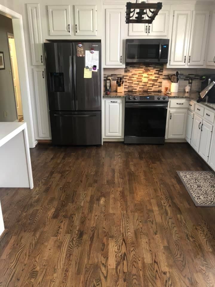 A kitchen with hardwood floors , stainless steel appliances , and white cabinets.