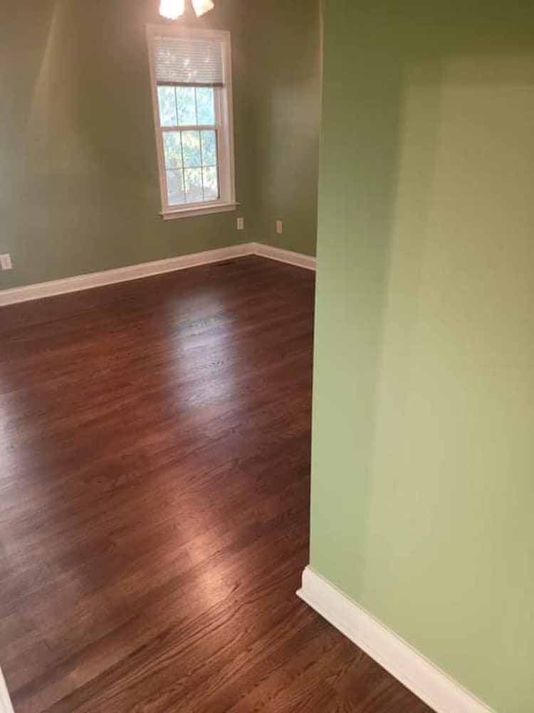 An empty living room with hardwood floors and green walls.
