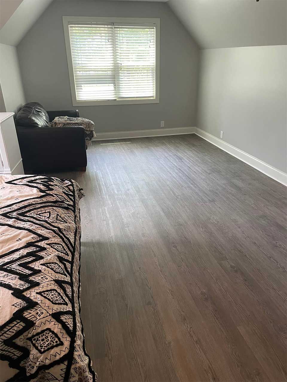 A bedroom with hardwood floors , a bed , a couch and a window.
