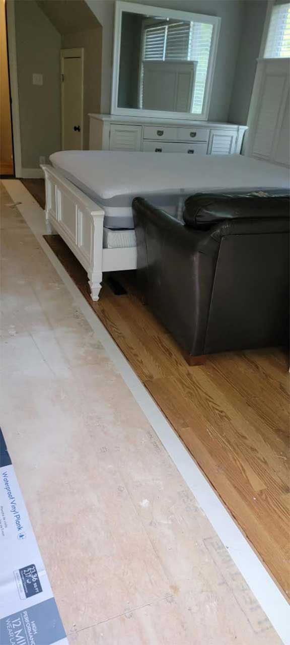 A bedroom with a bed , dresser , mirror and ottoman.